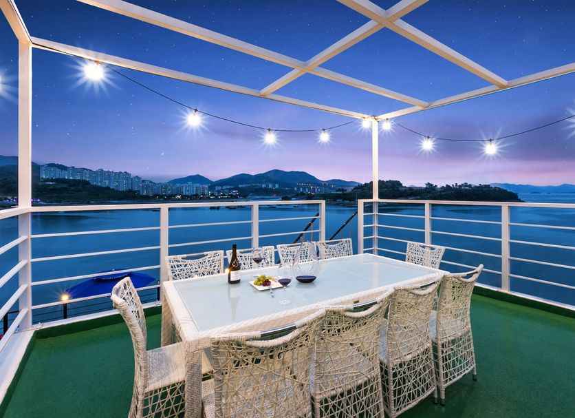 Onda D'oro Hostel Yeosu rooftop terrace with ocean view, dining table, and string lights at dusk