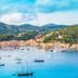 Hotel Plaza in Porto Azzurro overlooking a harbor with sailboats, colorful waterfront buildings, and hills