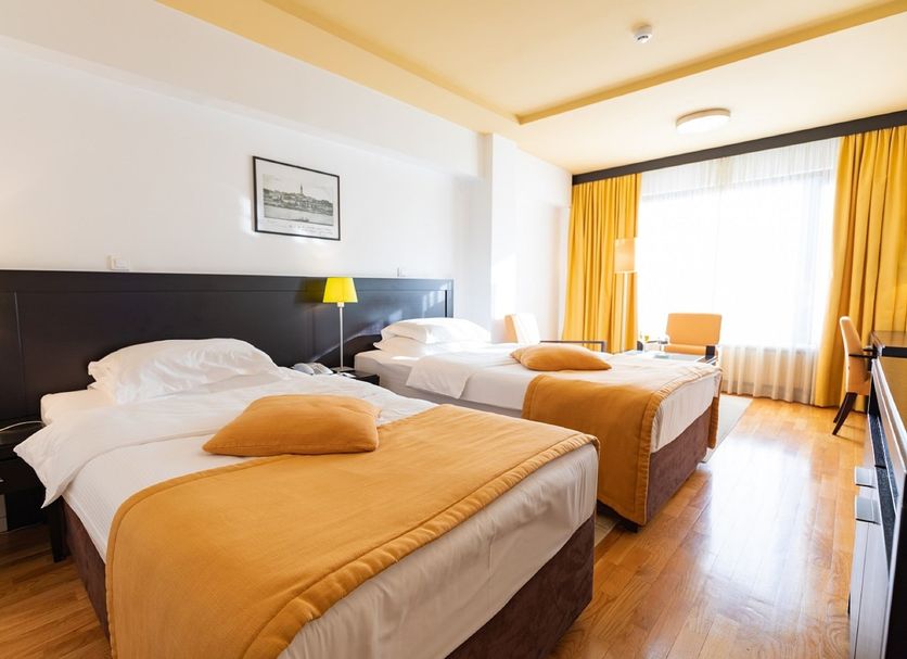 Hotel M Belgrade twin room with yellow bedding, bedside lamps, and bright window seating area