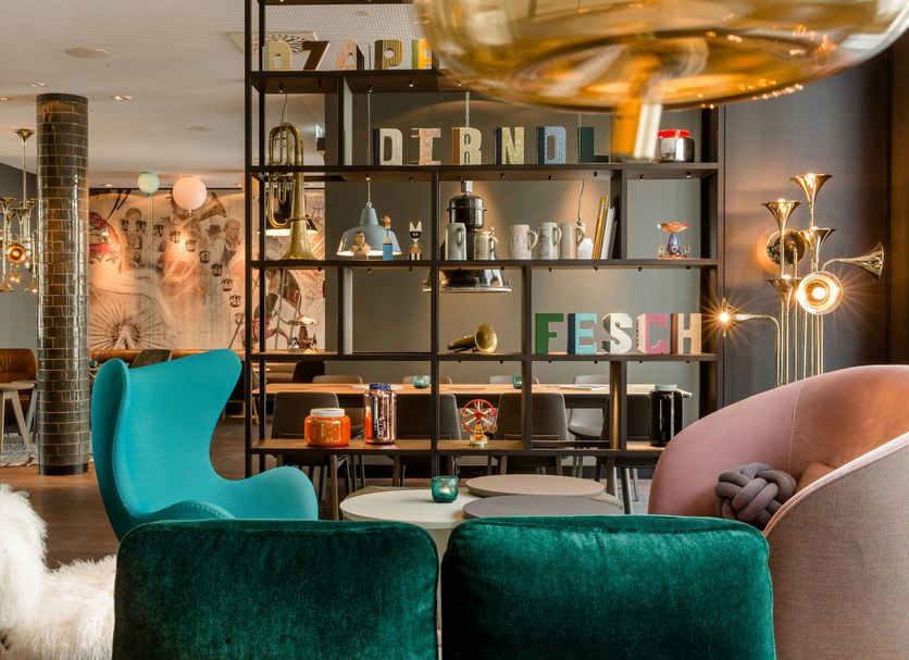 Motel One München-Westend lounge with velvet chairs, tables, and open shelving in Munich