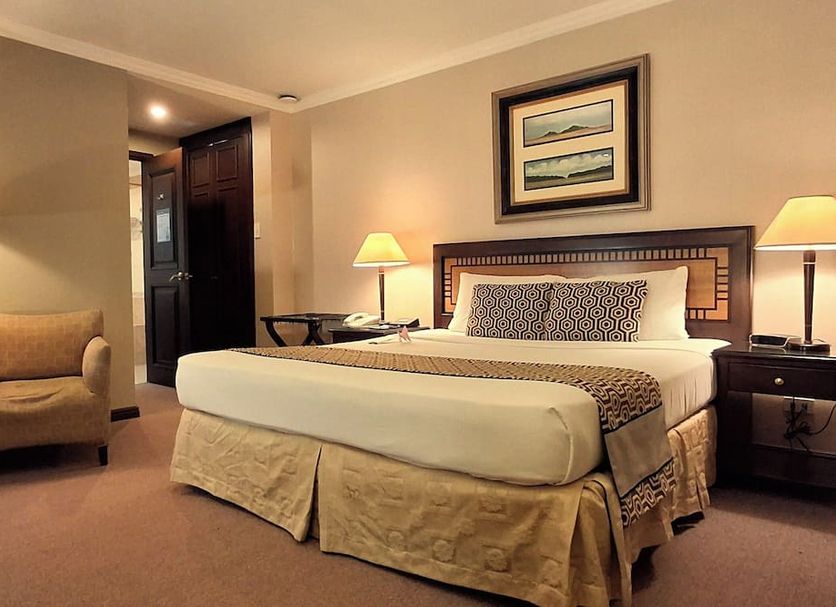 Herald Suites Solana Makati guest room with king bed, bedside lamps, armchair and framed wall art