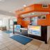 Motel 6 El Paso - Southeast lobby with front desk, orange accent wall, blue rugs, and seating area