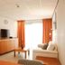 Studio's De Vlijt Texel in De Cocksdorp: bright suite with sofa, TV, coffee table and orange curtains