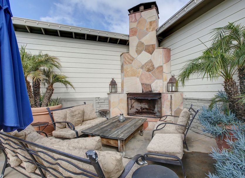 The Tides Laguna Beach outdoor patio with stone fireplace, seating, potted palms and umbrellas