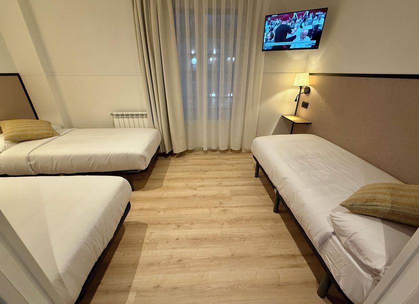 Muchomadrid Madrid room with three single beds, TV, lamp and window with sheer curtains
