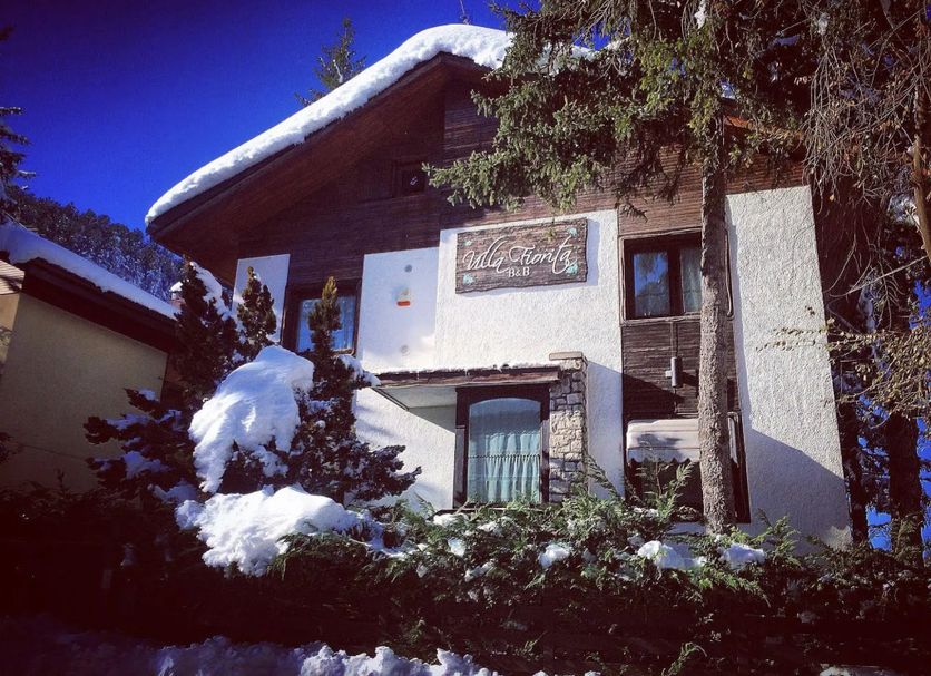 Villa Fiorita in Roccaraso, snow-covered chalet exterior with trees and blue sky