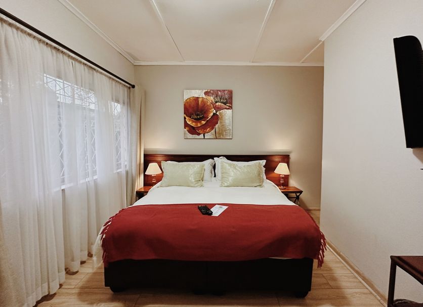 Malcolm Lodge Harare guest room with double bed, red throw, and sheer-curtained window