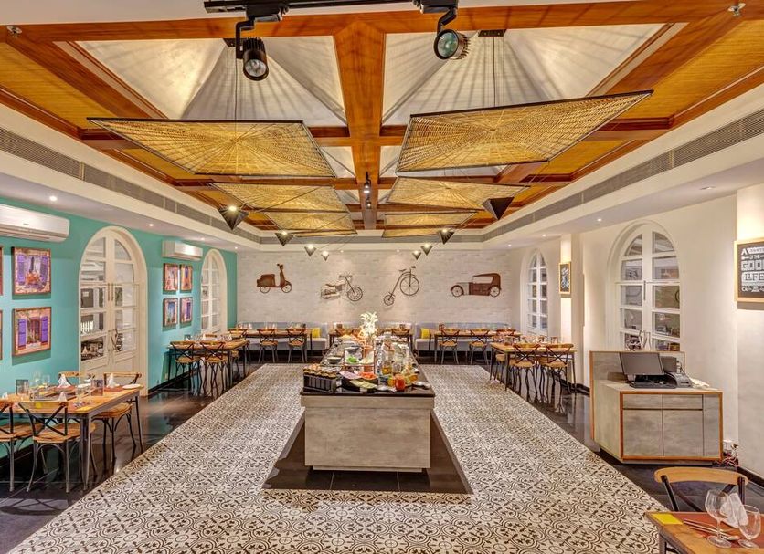 Club Mahindra Emerald Palms, Goa in Varca: bright restaurant with buffet island, patterned aisle and wood-beam ceiling