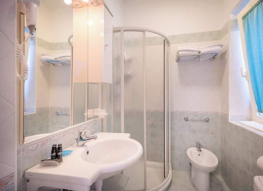 Hotel All'Orologio bathroom in Caorle with shower, sink, bidet and blue window curtain