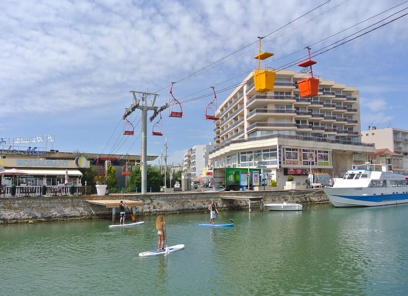 Hotel Amerique in Palavas-les-Flots with canal paddleboarders, boats and a cable car overhead