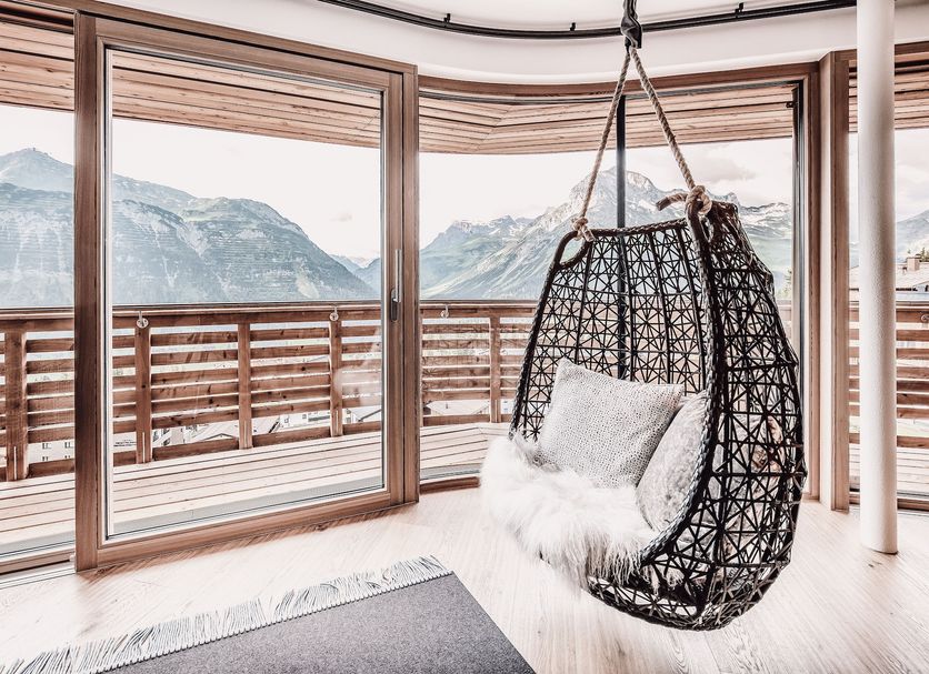 Hotel Goldener Berg in Lech am Arlberg: hanging chair beside panoramic mountain-view windows