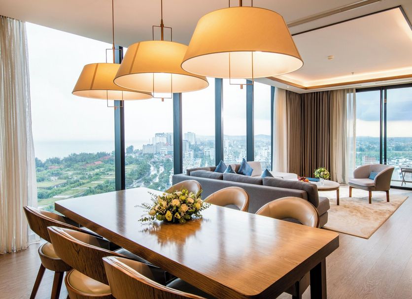 FLC Grand Hotel Samson in Sam Son suite with dining table, sofa, and panoramic ocean and city views