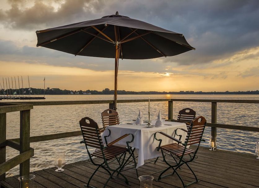 Romantik Hotel Jagdhaus Eiden am See in Bad Zwischenahn: lakeside terrace dining table under an umbrella at sunset