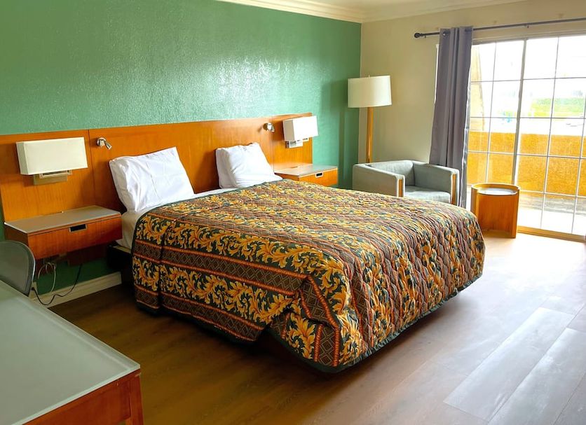 Relax Inn Los Angeles guest room with king bed, colorful quilt, armchair and balcony door