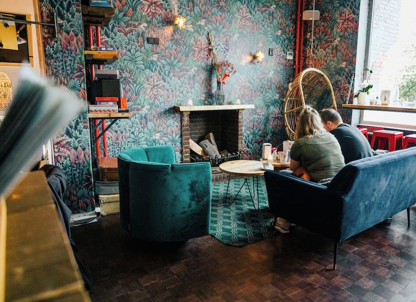 Hotel Credible Nijmegen lounge with floral wallpaper, fireplace, teal chairs and guests by the window
