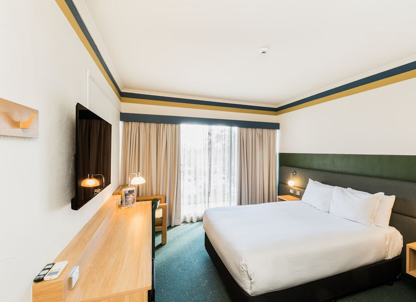 Statesman Hotel Canberra guest room with king bed, desk, wall-mounted TV and sheer-curtained window