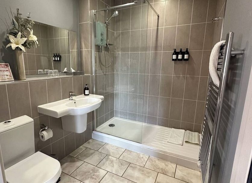 The Churchill Court, Woodstock: compact hotel bathroom with shower, wall-mounted sink, toilet and heated towel rail.