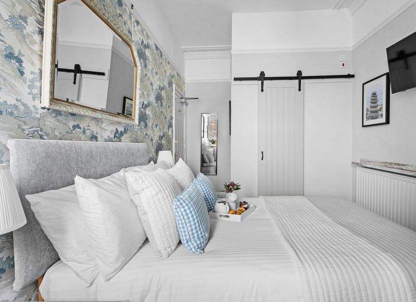 Sandway House Torquay bedroom with white bed, floral accent wall, wall mirror, and sliding closet doors
