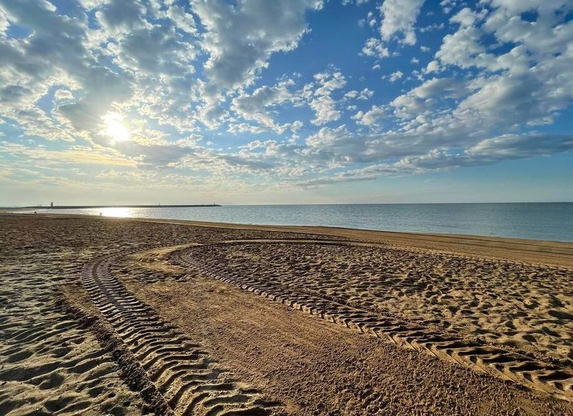 Hotel De La Plage in Valras-Plage with a sandy beach, tire tracks, and calm sea under a cloudy sky