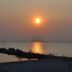 Sunset over calm water at Strandhotel Vigilante, Makkum, with a silhouetted shoreline and pier.