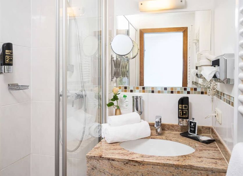 Arthotel ANA Gold Augsburg bathroom with glass shower, granite sink vanity, and wall mirror