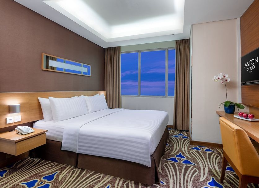 Aston Solo Hotel guest room with king bed, ocean blue window view, desk, and patterned carpet in Surakarta City