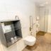 Hotel Herbers Efemir Gmbh bathroom with wall-mounted toilet, glass shower and sink in Südbrookmerland