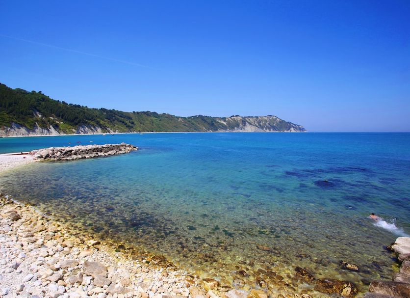 Fortino Napoleonico in Portonovo with clear turquoise sea, rocky beach, and coastal hillside view
