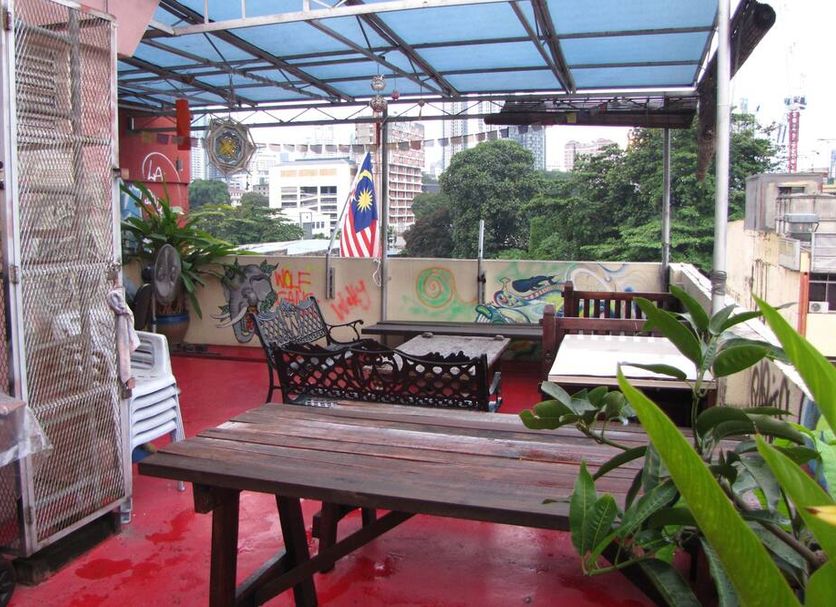 Oasis Guest House Kuala Lumpur rooftop terrace with wooden tables, chairs, plants and city views