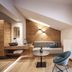 Hotel Lener in Mauls: modern suite with sloped ceiling, seating area and bedroom visible through glass door