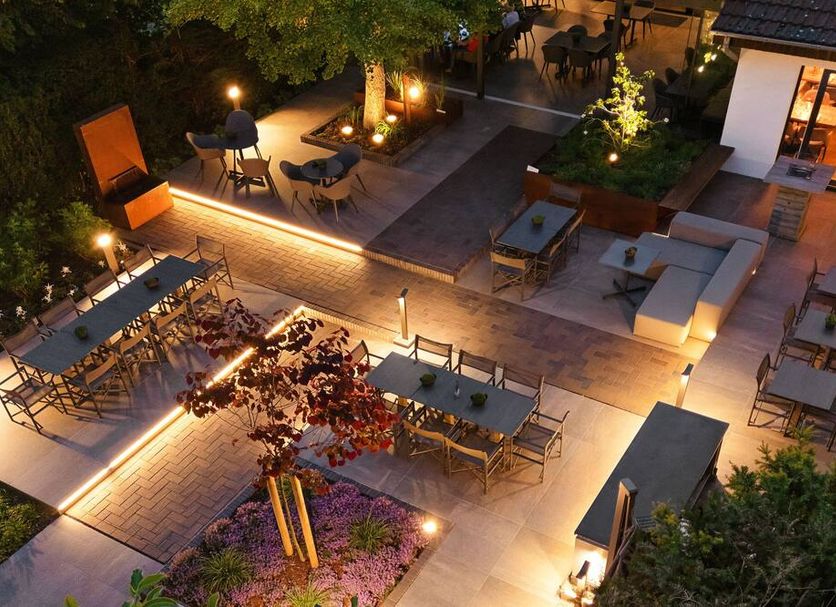 Hotel Tiek in Meppen: illuminated outdoor terrace with dining tables and lounge seating at night