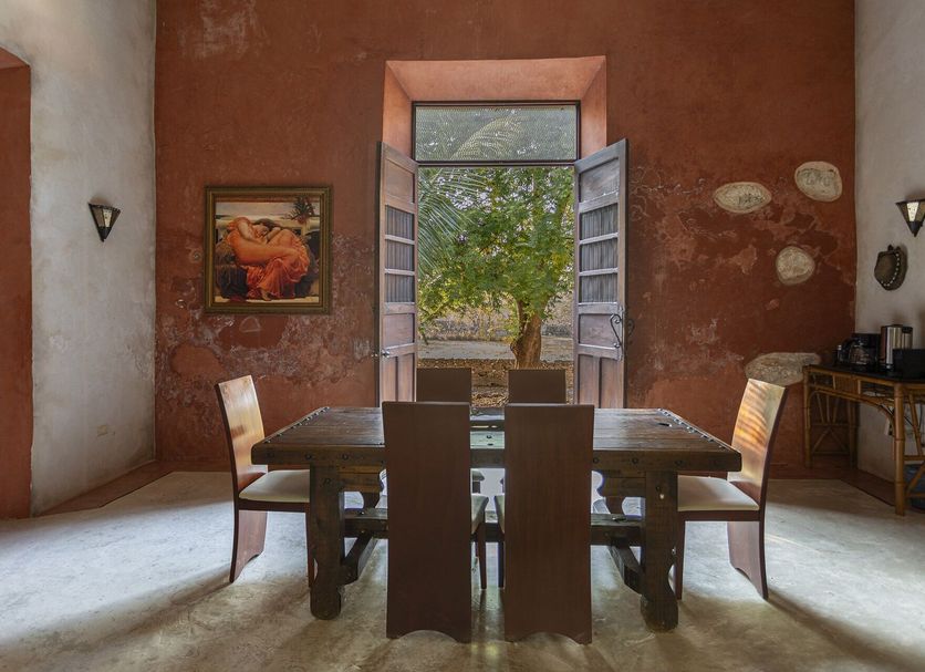 Hacienda Sacnicte in Izamal dining room with open doors, courtyard tree view, and rustic decor