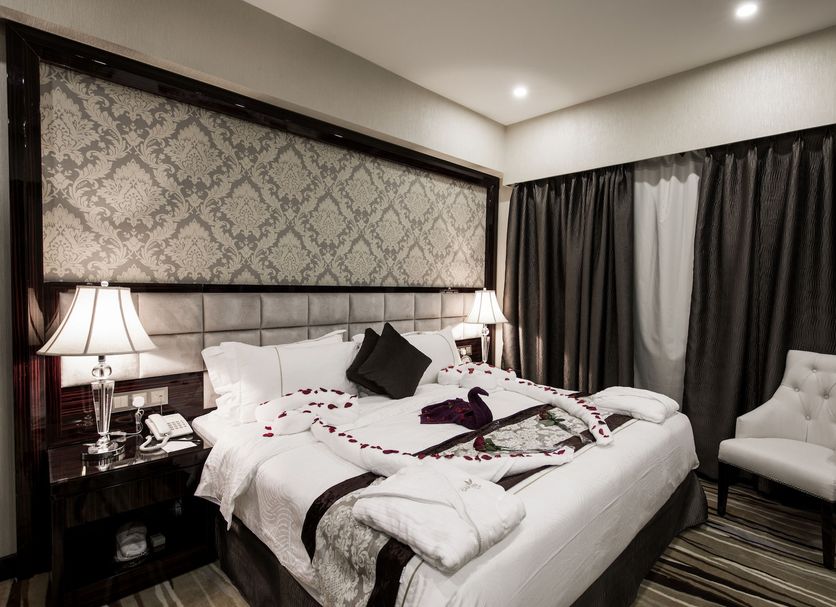 Al Muhaidb Residence Al Ahsa in Hofuf: elegant hotel room with king bed, lamps, and lounge chair