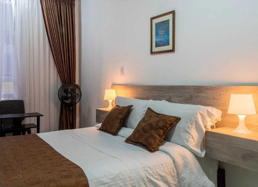 Hotel Cafetto in Pereira guest room with bed, bedside lamps, desk and large window with curtains