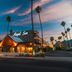 Royal Sun Palm Springs exterior at dusk with glowing entrance and tall palm trees in Palm Springs