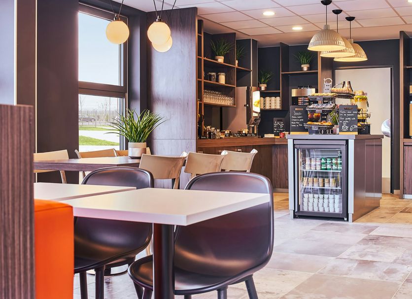 easyHotel Paris Charles de Gaulle Villepinte breakfast area with tables, chairs and café counter in Tremblay-en-France