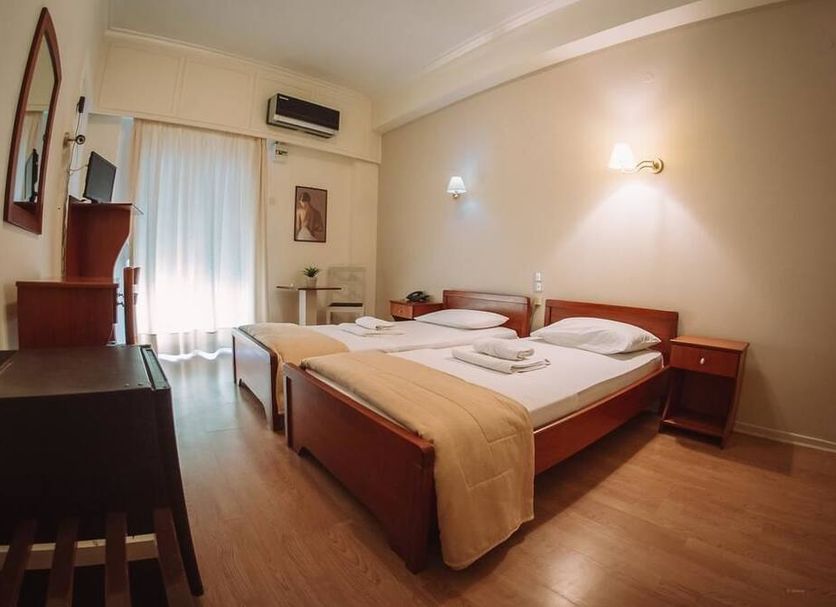 Hotel King Pyrros in Ioánnina: simple twin-bed guest room with desk, wood floors, and balcony door