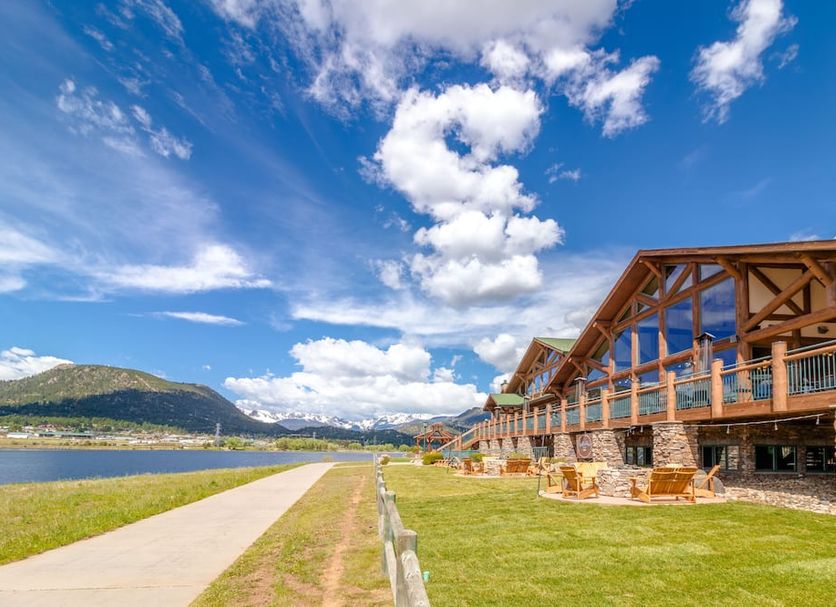 The Estes Park Resort in Estes Park with lakeside lawn, walkway, and mountain views under a blue sky