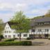 Haus Dumicketal in Drolshagen, white 3-story hotel with balconies and parked scooters beside trees