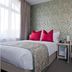 W12 Rooms London guest room with double bed, pink pillows, desk, and large window