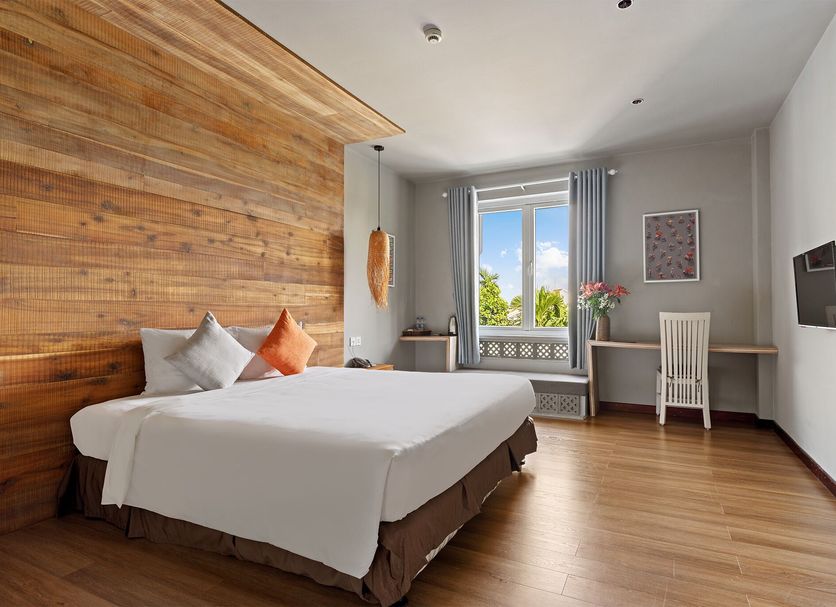 Goda Boutique Hotel Hoi An room with wooden accent wall, bed, desk, and window view