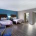 Motel 6 Burlington NC room with two beds, blue accent wall, sofa, and wood-look flooring in Burlington