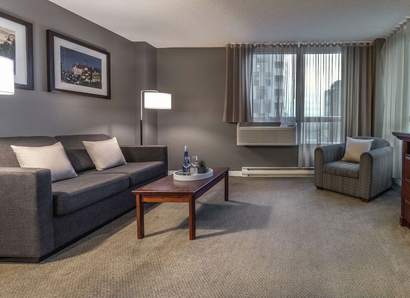 Hotel Faubourg Montreal guest room with sofa, armchair, coffee table and city-view window