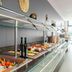 Staycity Aparthotels Heidelberg buffet counter with fruit, pastries, and bottles in a bright dining area
