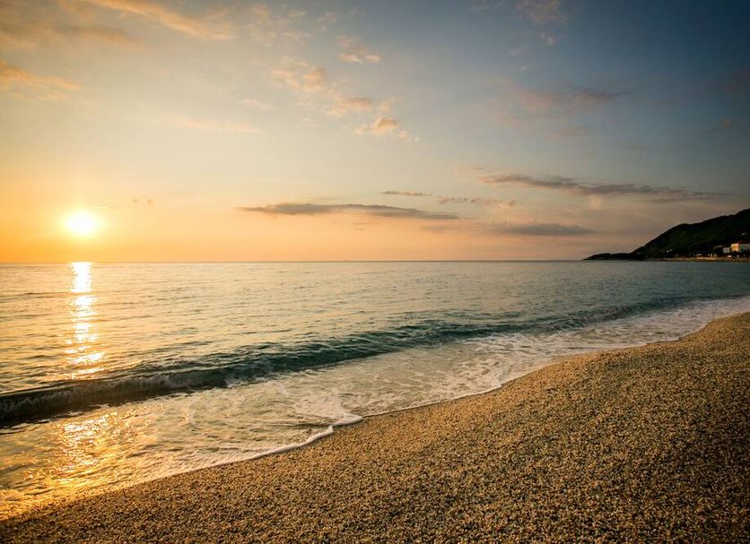 Sunset over the beach at Kenta Beach Hotel in Agios Ioannis, with calm sea and shoreline.