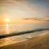 Sunset over the beach at Kenta Beach Hotel in Agios Ioannis, with calm sea and shoreline.