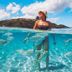 Barefoot Kuata Island on Kuata Island: woman standing in clear turquoise ocean with island backdrop