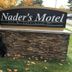 Nader's Motel & Suites sign in Ludington with guests standing beside it on a grassy lawn