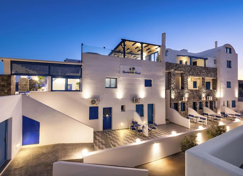 Honeymoon Beach Studios in Perissa at dusk, with lit white terraces and sea-view balconies