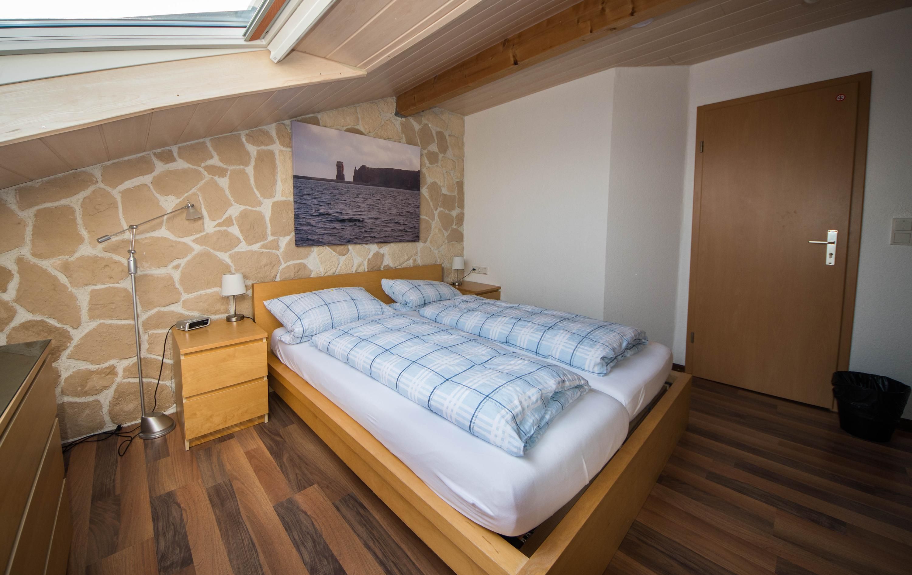 Hotel Panorama Garni in Heligoland bedroom with skylight, wood bed, stone accent wall and sea photo